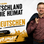 Peter Schreiber vor einer gelben Fahne mit der Aussage: „Heimat ist nicht beliebig. Deutschland ist die Heimat der Deutschen.“