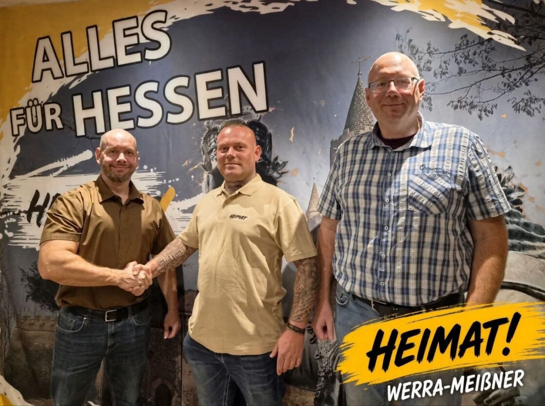 Drei Vertreter der Partei Die Heimat Werra-Meißner-Kreis stehen vor einer Wandaufschrift mit der Losung „Alles für Hessen“.
