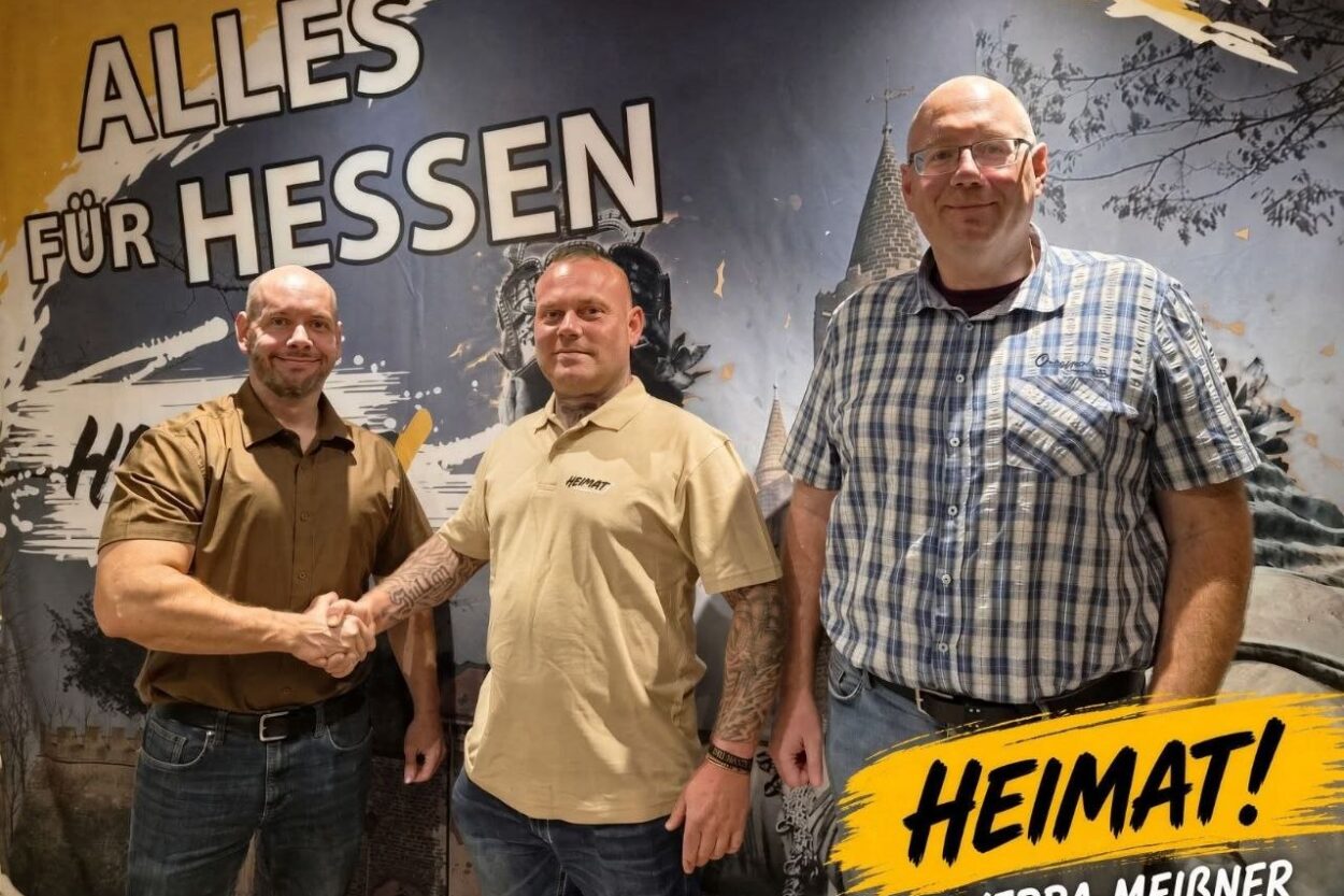 Drei Vertreter der Partei Die Heimat Werra-Meißner-Kreis stehen vor einer Wandaufschrift mit der Losung „Alles für Hessen“.